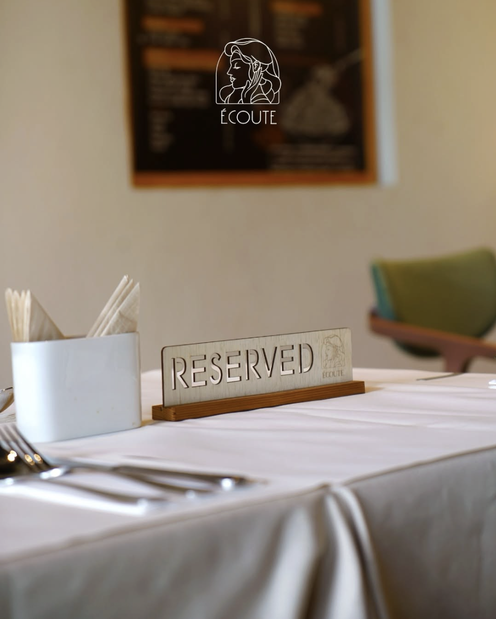 Écoute reserved sign on a white linen table with softly lit dining chairs behind it